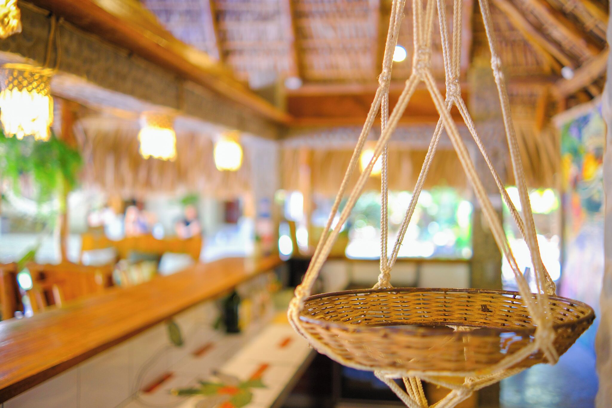 Una cesta colgante de mimbre en un restaurante con mostrador de madera y techo de paja.