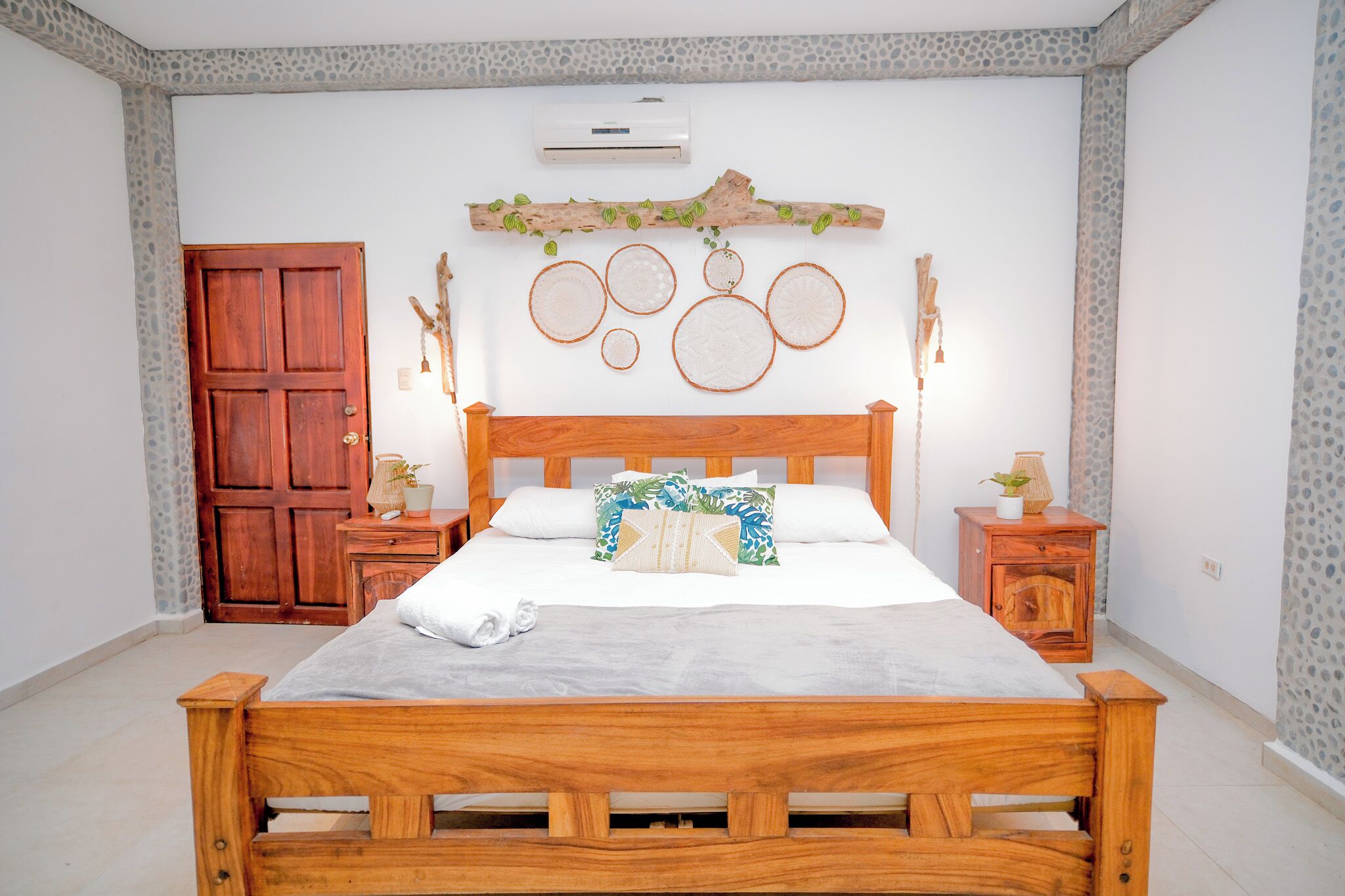 Un letto di legno con materasso bianco, due comodini, un armadio in legno, una parete con motivo in pietra e un condizionatore d'aria.