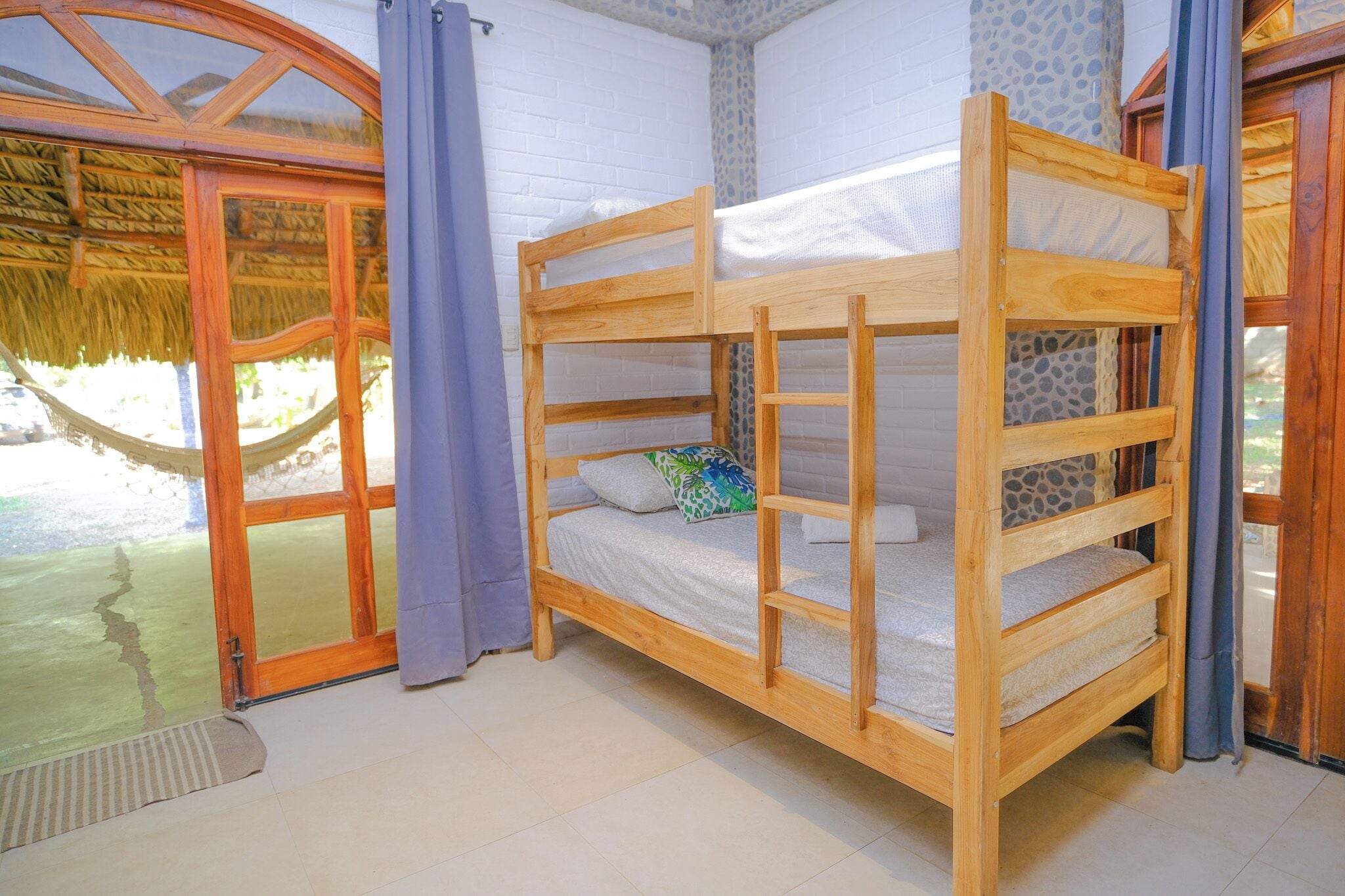 Ein Stockbett mit Holzrahmen und Matratze, eine Glastür, die nach draußen führt, und eine Wand mit Muster.