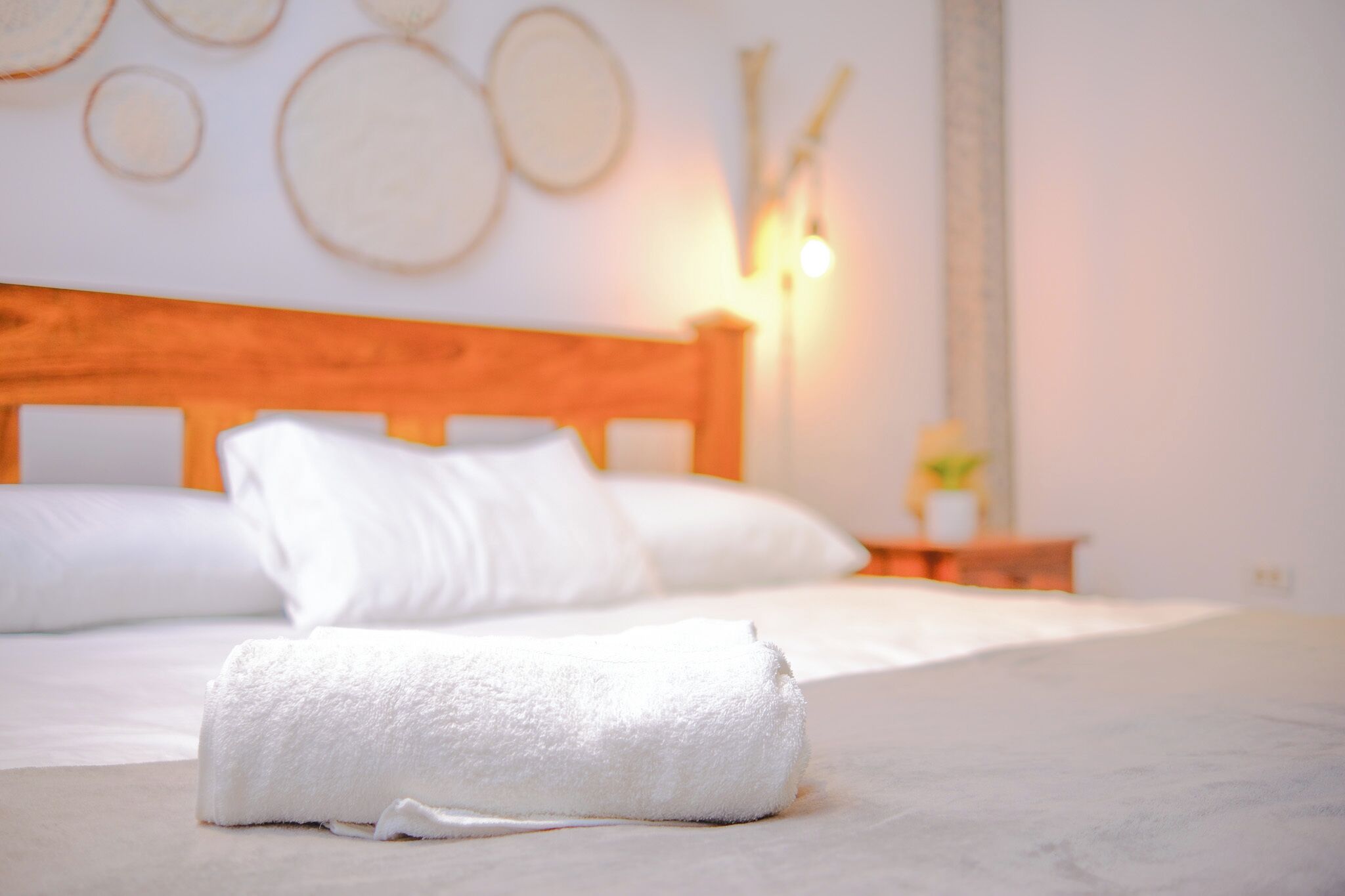 Una cama bien hecha con sábanas blancas y una toalla blanca enrollada al frente.