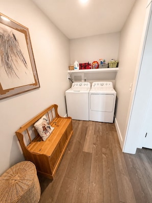 A laundry room with two washing machines, a bench, and a shelf with laundry supplies. - Sebago Lake Estate, 300’ Frontage, Inside the State Park, Private Dock & Kayaks (Casco)