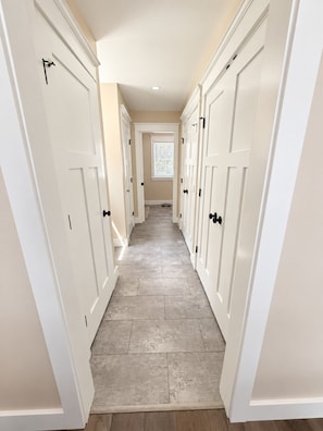 A narrow hallway with white doors on both sides, leading to a room with a window and a ceiling light. - Sebago Lake Estate, 300’ Frontage, Inside the State Park, Private Dock & Kayaks (Casco)