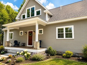 A two-story house with a covered porch, stone pillars, and a front door with a wreath. - Sebago Lake Estate, 300’ Frontage, Inside the State Park, Private Dock & Kayaks (Casco)