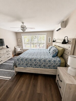 Ein Schlafzimmer mit einem Bett, einem Sessel, einem Schreibtisch, einem Deckenventilator und einem Fenster mit Jalousien.