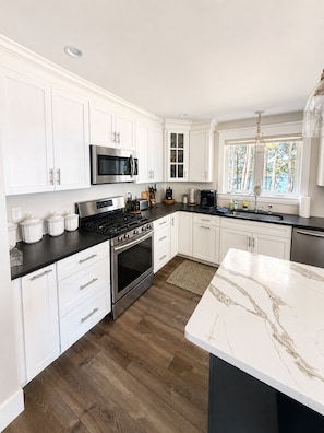 A modern kitchen with white cabinetry, a stainless steel stove, and a marble countertop. - Sebago Lake Estate, 300’ Frontage, Inside the State Park, Private Dock & Kayaks (Casco)