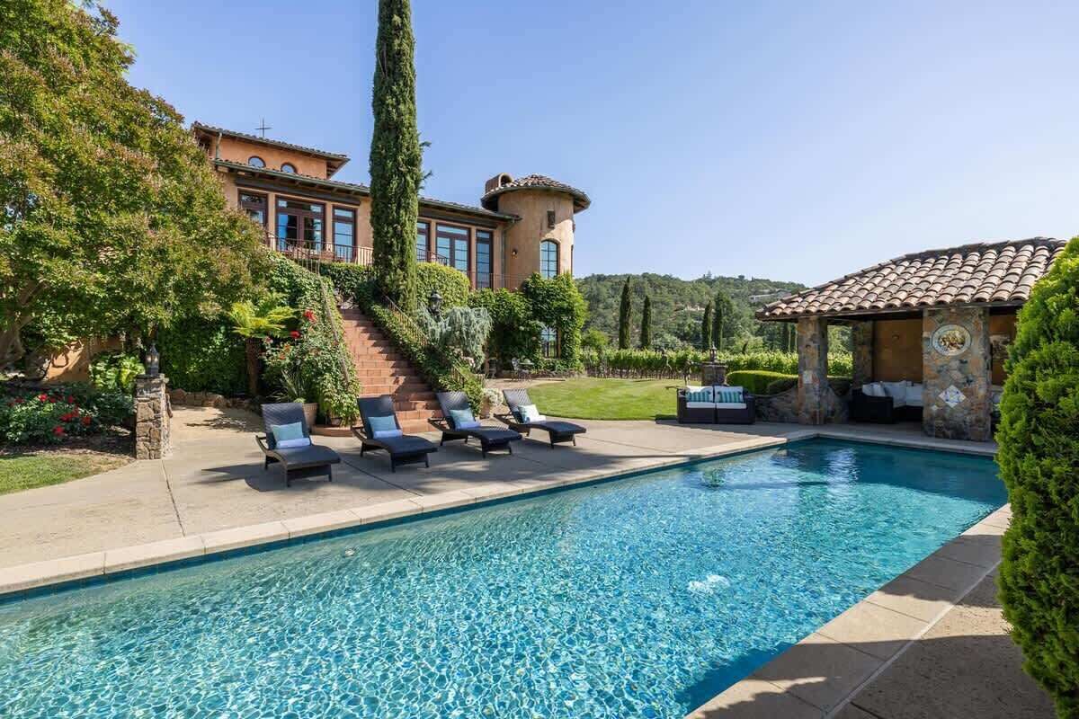 Una piscina con sillas de descanso, un edificio de piedra y un jardín cuidado.