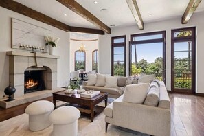A spacious living room with a fireplace, a sofa set, and large windows offering a view of the outdoors. - Hagen Heights Vineyard Estate Napa Valley (Napa)