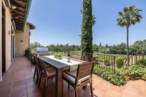 Eine Terrasse im Freien mit Tisch und Stühlen, einem Grill und Blick auf einen Weinberg.