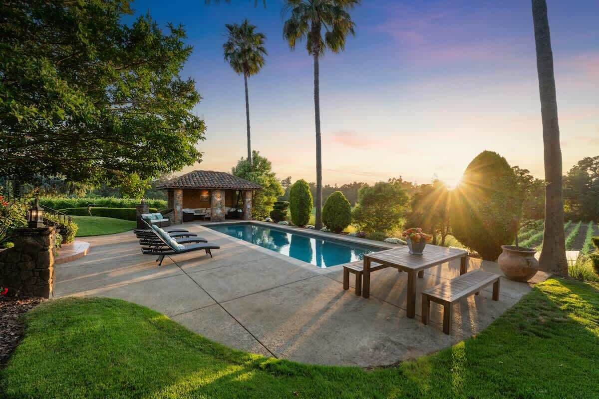 A swimming pool with lounge chairs and a table, surrounded by greenery and palm trees.