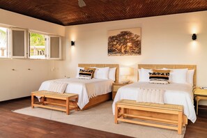 A hotel room with two beds, a wooden bench, a painting of trees, and a window with a view of greenery. - Bay Low House, a luxurious all-inclusive beachfront property. (La Ribera)