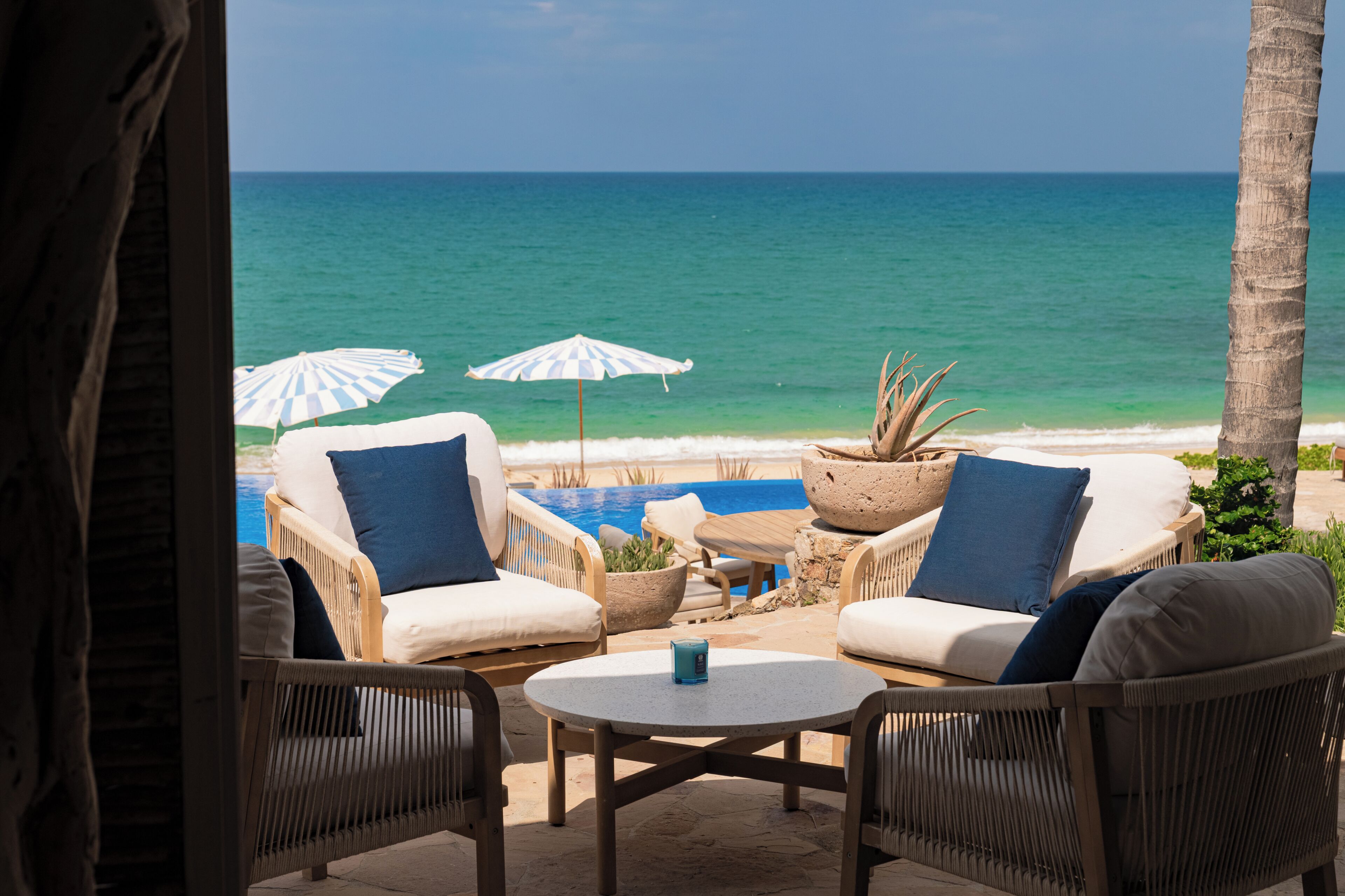 An outdoor seating area with wicker chairs and a table, overlooking a pool and the ocean.