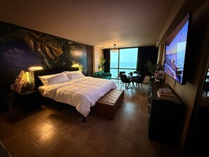 A hotel room with a large bed, a desk, a chair, a television, and a view of the sea. - The Love Den | Oceanfront Couples Retreat (Daytona Beach)
