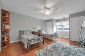A bedroom with two beds, a ceiling fan, a bookshelf, a window with blinds, and a door. - Hudson River views with pool and hot tub (Kingston)