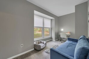 A room with a large window, a desk with a chair, a blue sofa, and a pet bed. - Hudson River views with pool and hot tub (Kingston)