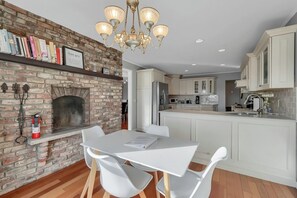 Een moderne keuken met een metselwerk open haard, witte kastjes en een eethoek met een witte tafel en stoelen.