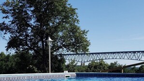 Una piscina con agua azul cristalina, rodeada de árboles y un puente al fondo.