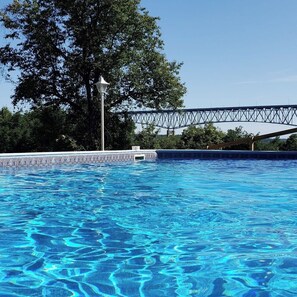 Ein Schwimmbad mit klarem, blauem Wasser, umgeben von Bäumen und einer Brücke im Hintergrund.