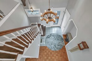 Eine Treppe mit Holzbodenstufen und weißen Balustraden, eine Kandelaber und ein runder Teppich sowie eine Uhr an der Wand.
