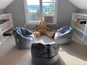 Ein Zimmer mit großem Fenster, zwei Sitzsäcken, einem Teddybären und Regalen mit Büchern und Spielen.