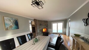 Un comedor con una mesa larga, sillas negras, una chimenea de piedra y vistas a través de un ventanal.