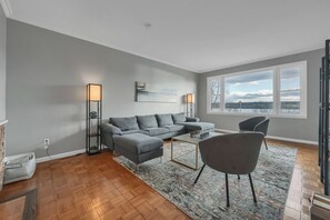 Ein modernes Wohnzimmer mit einem grauen Sofa, einem Couchtisch und Seeblick durch große Fenster.