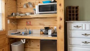 A compact kitchen with wooden cabinetry, a microwave, a sink, and a small refrigerator. - Cabin#6 in Lake George Cabins & RV Park (Lake George)