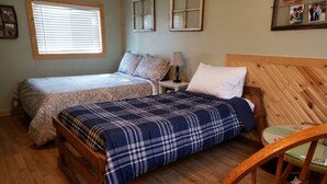 A bedroom with two beds, a wooden headboard, a nightstand, and a chair. - Cabin#6 in Lake George Cabins & RV Park (Lake George)