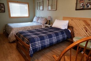 A bedroom with two beds, a wooden headboard, a nightstand, and a chair. - Cabin#6 in Lake George Cabins & RV Park (Lake George)