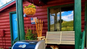 A barbecue grill on a porch with a bench and an owl decoration. - Cabin#6 in Lake George Cabins & RV Park (Lake George)