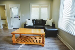 Ein Wohnzimmer mit Couchtisch aus Holz, einer schwarzen Ledersofa und einer Tür mit Milchglasfenster.