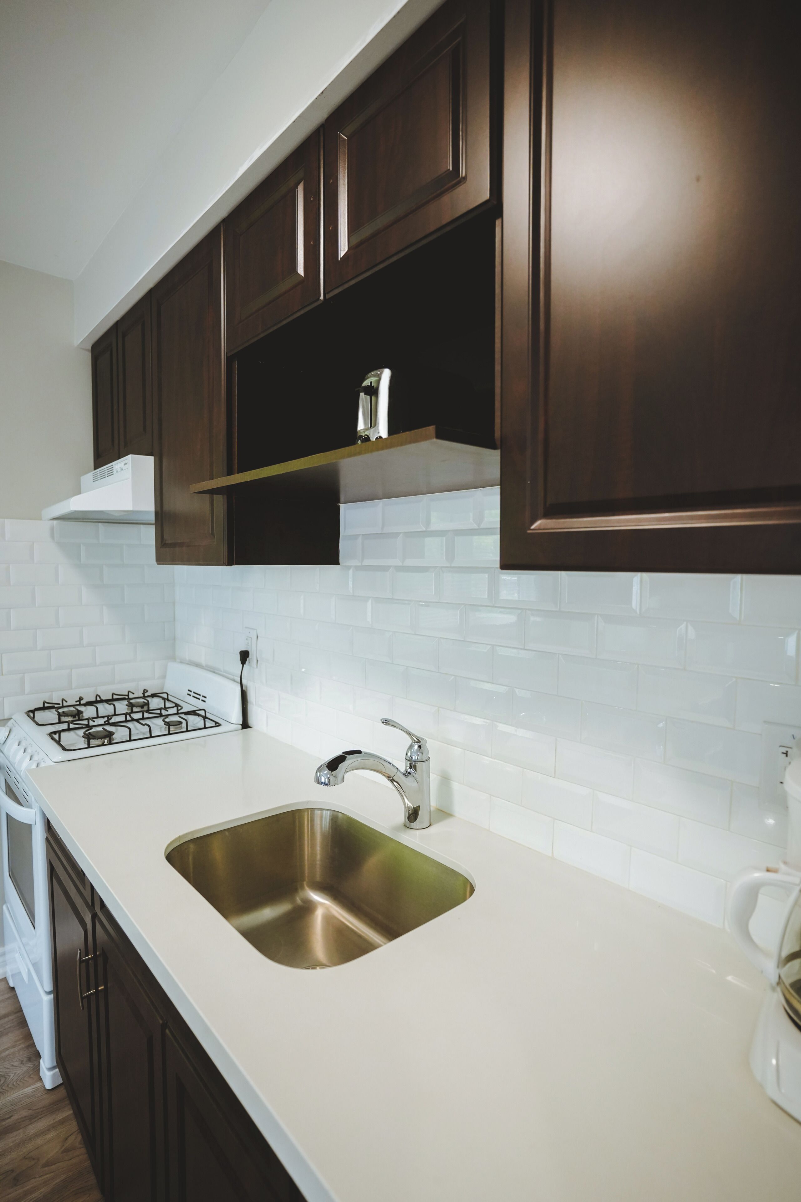 A kitchen with dark wooden cabinets, a white countertop, a stainless steel sink, and a gas stove.