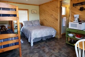 Een gezellige kamer met een stapelbed, een bed met beddengoed met een patroon, een groene plank met keukengerei en een magnetron op een houten tafel.