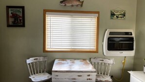 Ein Zimmer mit Fenster, einem an der Wand befestigten Fisch, einer alten Klimaanlage und einem Tisch mit Stühlen.