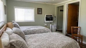 Un dormitorio con dos camas, un ventilador de techo, una ventana con persianas, un calefactor y una silla.