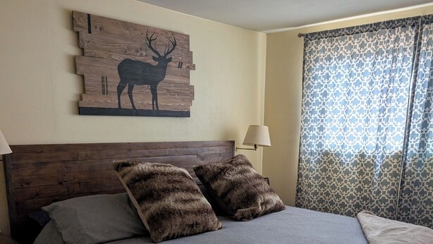 Una camera da letto con una testiera in legno, due cuscini soffici, una coperta, una lampada e un quadro raffigurante un cervo.