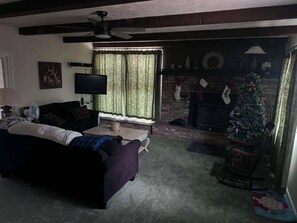 Ein Wohnzimmer mit einem dunkelgrauen Sofa, einem Fernseher, einem Kamin und einem Weihnachtsbaum.