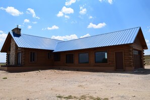 A log cabin with a metal roof, multiple windows, and a stone chimney.