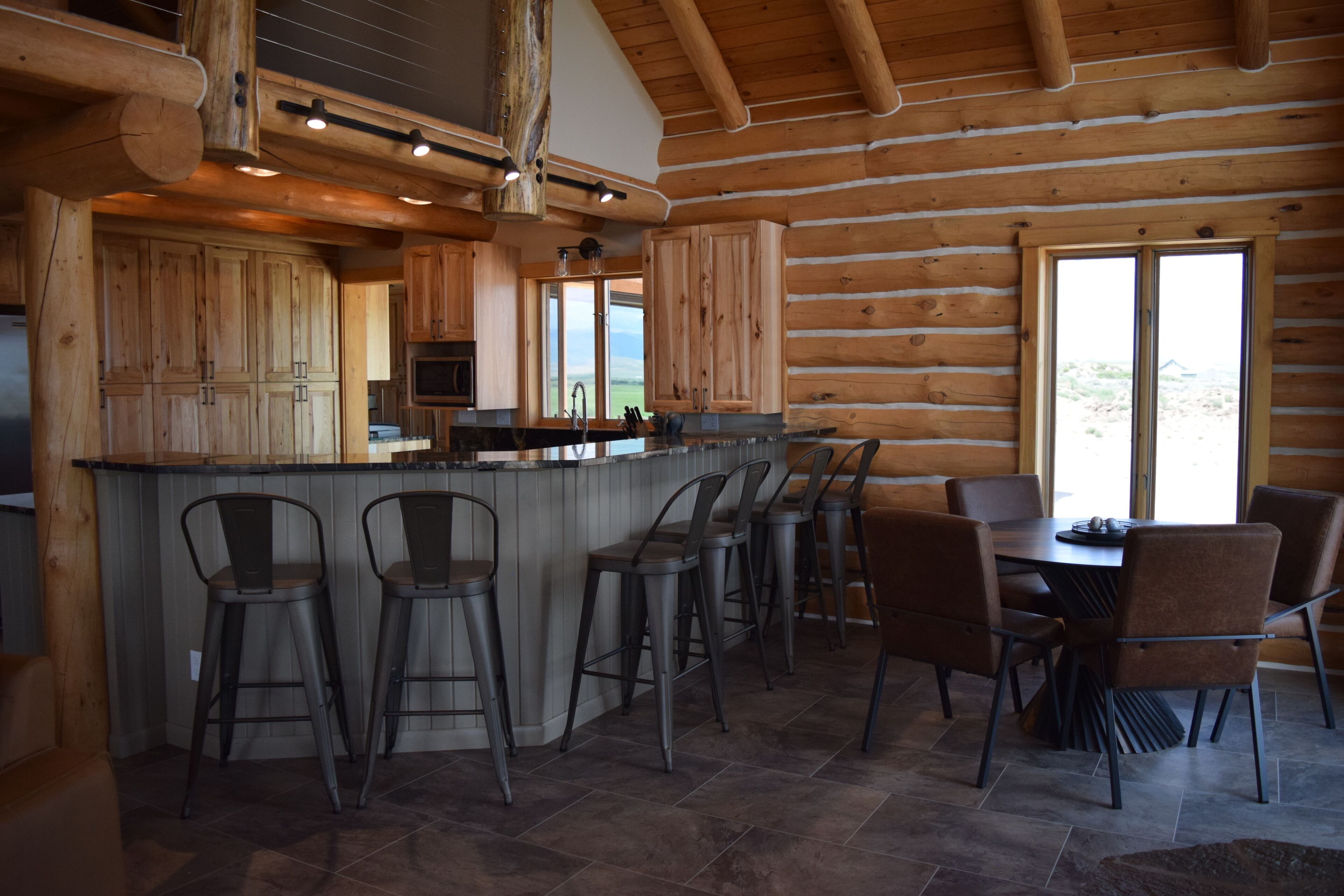 A log cabin interior with a bar area, dining space, and large windows.