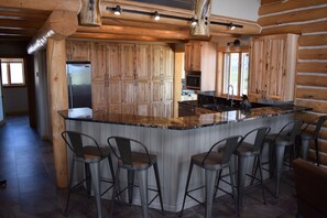 A kitchen with wooden cabinets, a stainless steel refrigerator, a microwave, and a large island with bar stools.