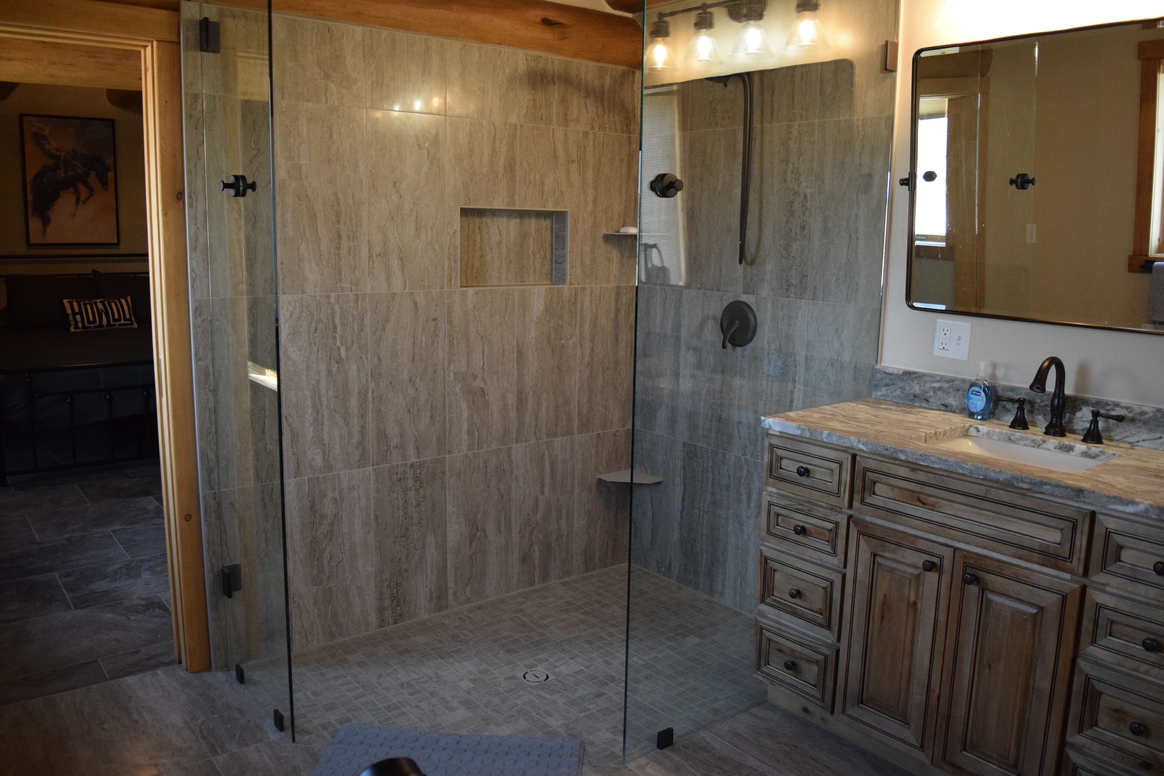 A bathroom with a glass shower enclosure, a wooden vanity with a sink, and a mirror above the vanity.