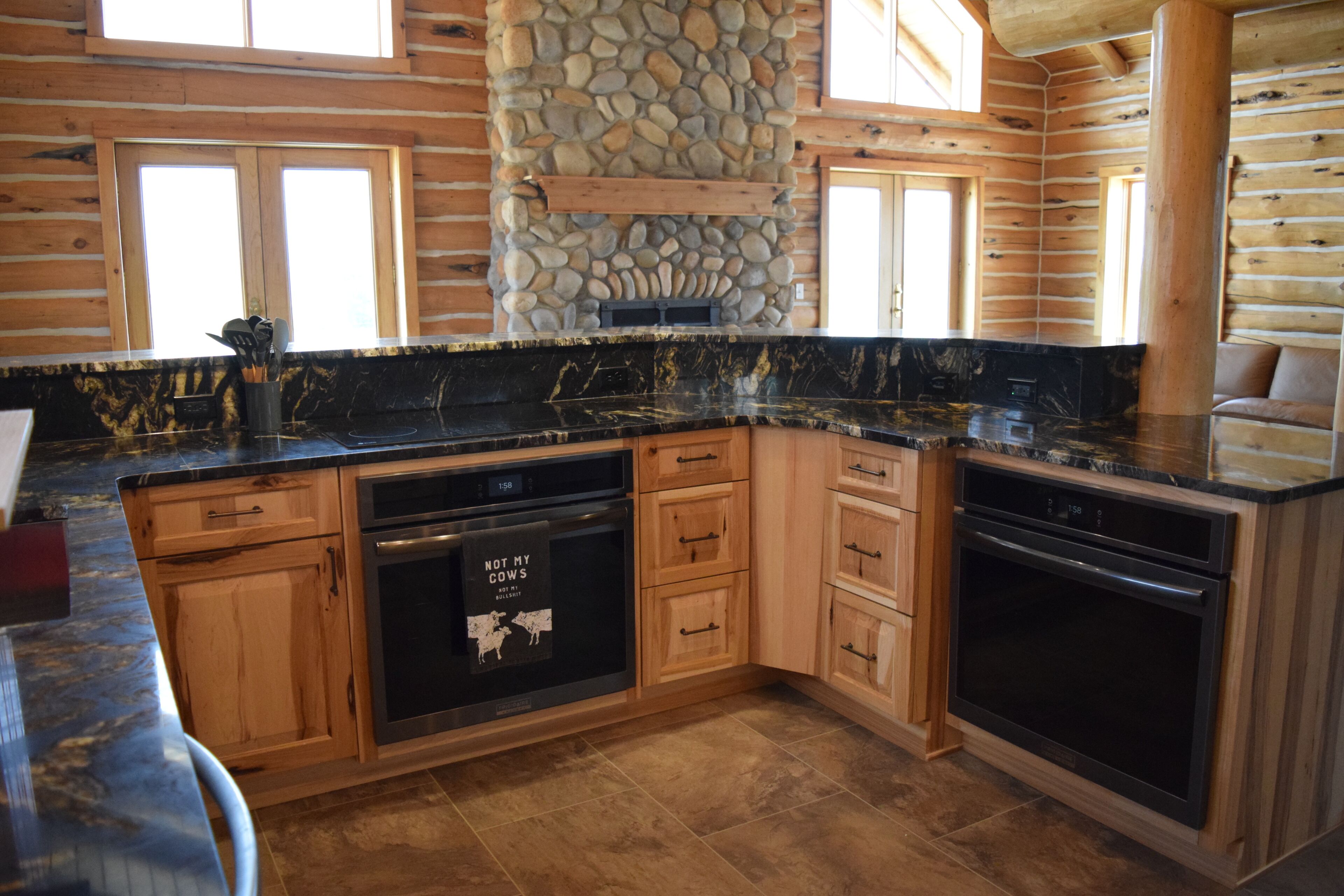 A kitchen with wooden cabinets, a stone accent wall, and a black countertop.