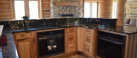 A kitchen with wooden cabinets, a stone accent wall, and a black countertop.