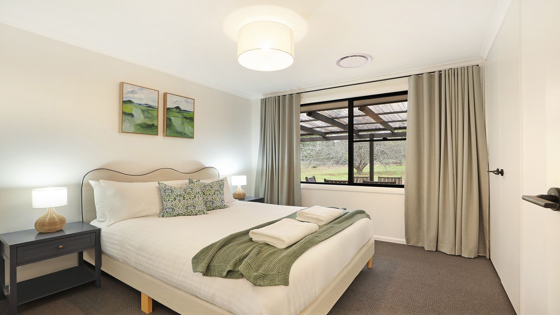 A well-lit bedroom with a large bed, a nightstand, a lamp, and a window with curtains.