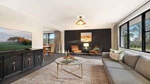 A modern living room with a flat-screen TV, a coffee table, a sofa, and a dining area with chairs.