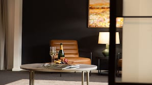 Ein Hotelzimmer mit Ledersessel, kleinem runden Tisch, Champagnerflasche, Gläsern und einer Obstplatte.