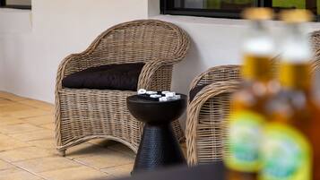 Wicker chairs with cushions, a small table with a black base, and a bottle in the foreground.