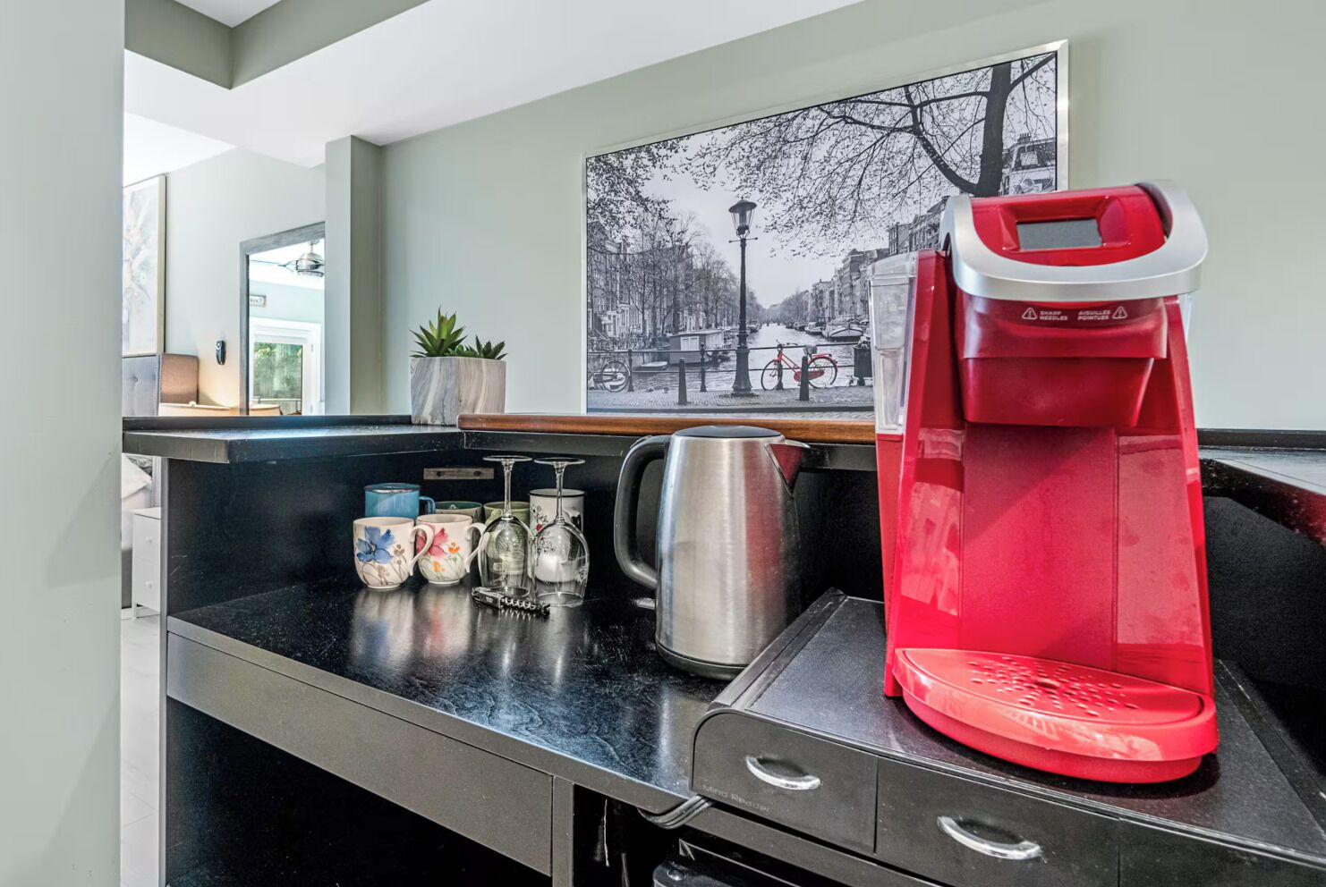 A kitchenette with a coffee maker, a kettle, and mugs on the counter.