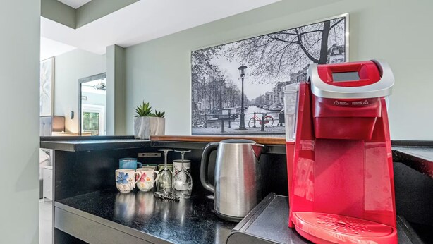 Una kitchenette con cafetera, hervidor y tazas sobre la encimera.