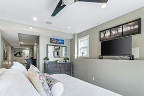A bedroom with a bed, dresser, TV, and a ceiling fan.