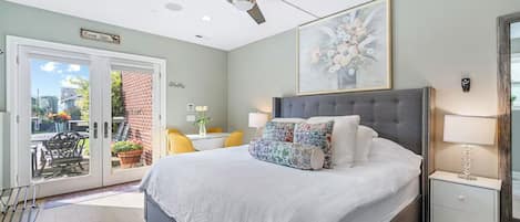 A bedroom with a bed, a ceiling fan, a nightstand, a lamp, and a view of the outside.
